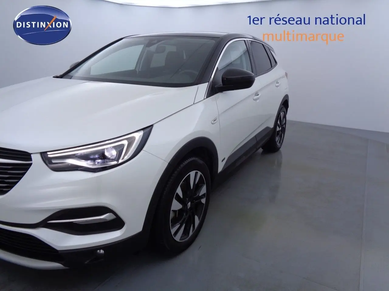 Vue 3/4 avant droit d’un Opel Grandland X blanc métal avec jantes bicolores et rétroviseurs noirs.