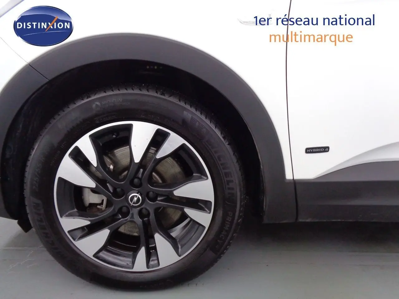 Gros plan sur la roue avant gauche d’un Opel Grandland X blanc métal avec badge Hybrid 4 visible sur la carrosserie.
