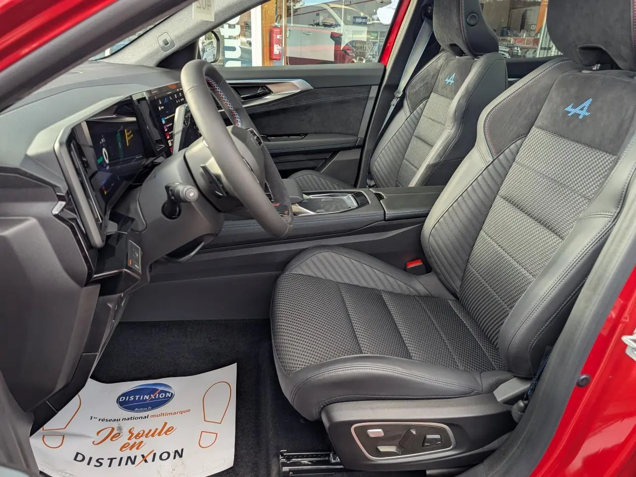 Vue intérieure côté conducteur du Renault Austral rouge, sièges en tissu carbone Alcantara avec logo Alpine bleu brodé.