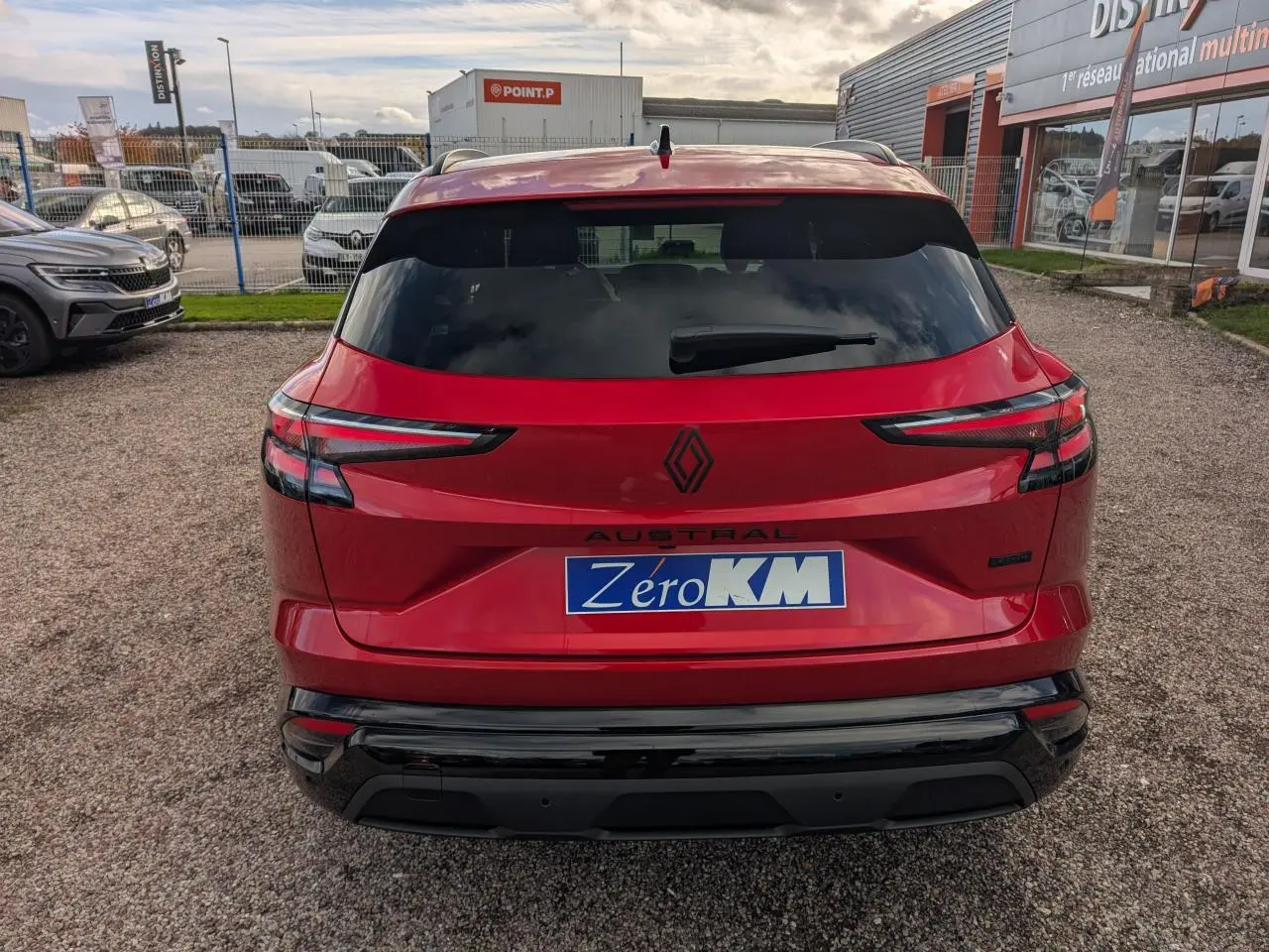Vue arrière d'un Renault Austral rouge métallisé avec logos noirs et hayon fermé sur un parking extérieur.
