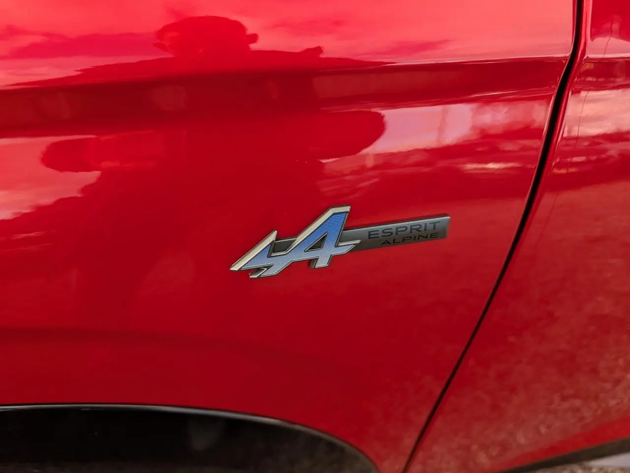 Gros plan sur l'écusson Esprit Alpine bleu et noir sur la porte rouge métallisée d'un Renault Austral 2025