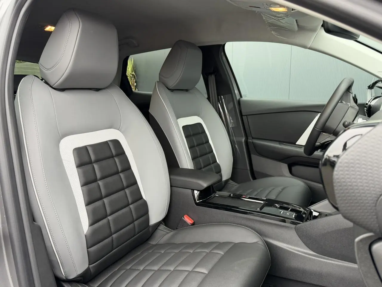 Vue intérieure côté gauche des sièges avant gris clair et noir de la Citroën C4 NV Hybrid 2025 avec accoudoir central.