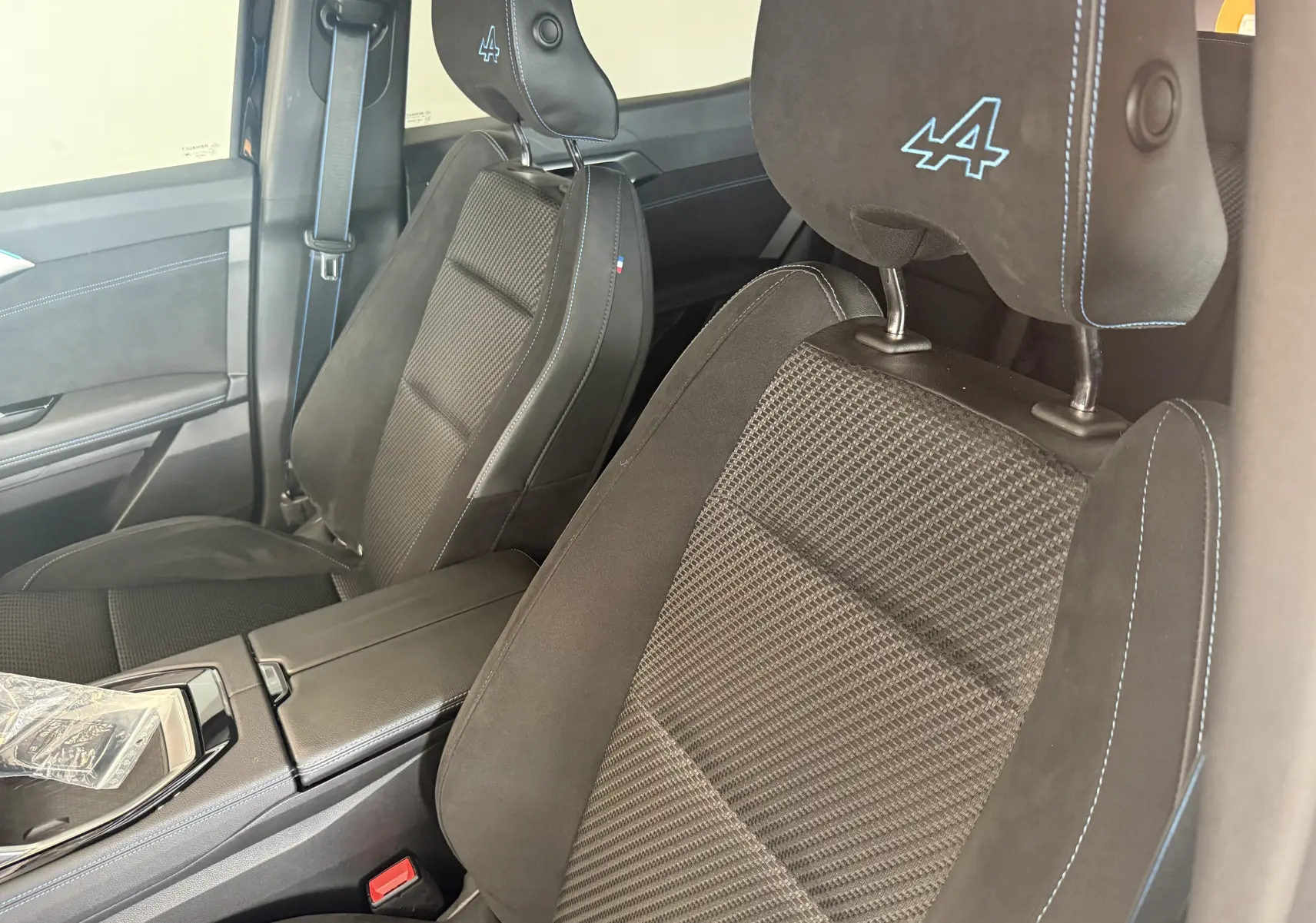 Gros plan sur les sièges avant en tissu mixte/Alcantara noir avec surpiqûres bleues et logo Alpine brodé sur appuie-tête.