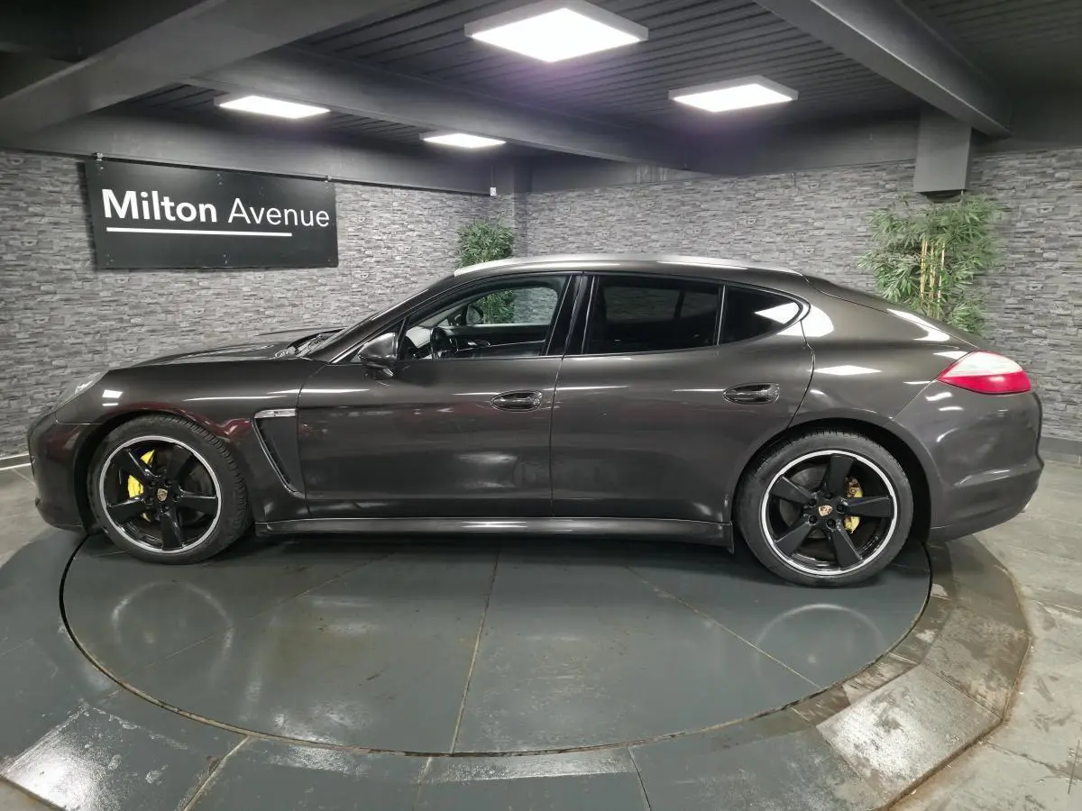 Vue de profil côté gauche d'une Porsche Panamera marron métallisée avec jantes noires sport 20 pouces dans un showroom.