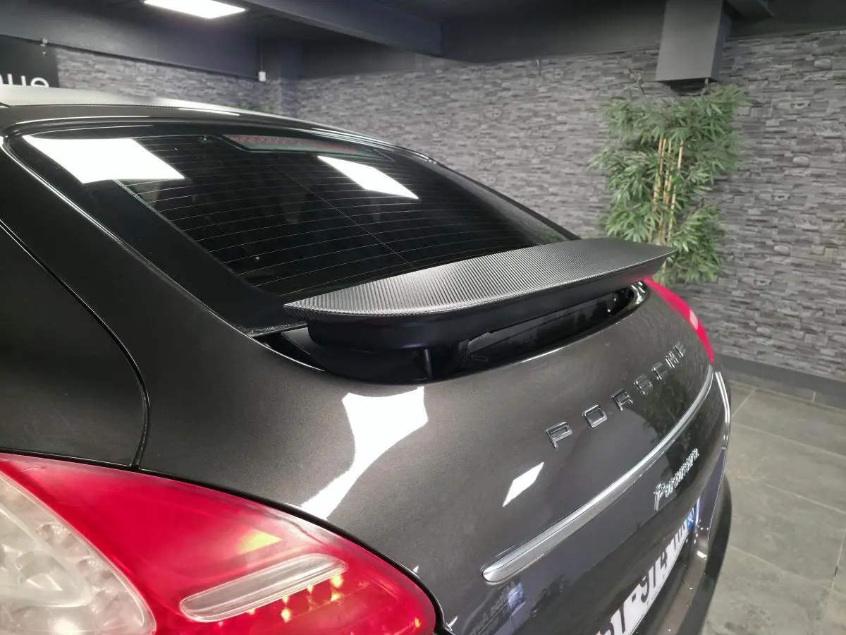 Vue arrière 3/4 droite d'une Porsche Panamera marron avec aileron télescopique déployé et feux arrière rouges.
