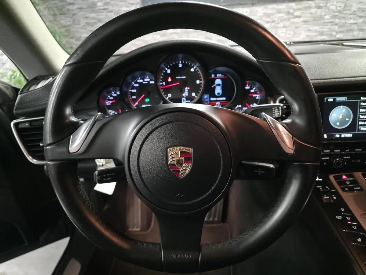 Vue intérieure centrée sur le volant cuir noir de la Porsche Panamera 2011 avec tableau de bord et instruments ronds éclairés.