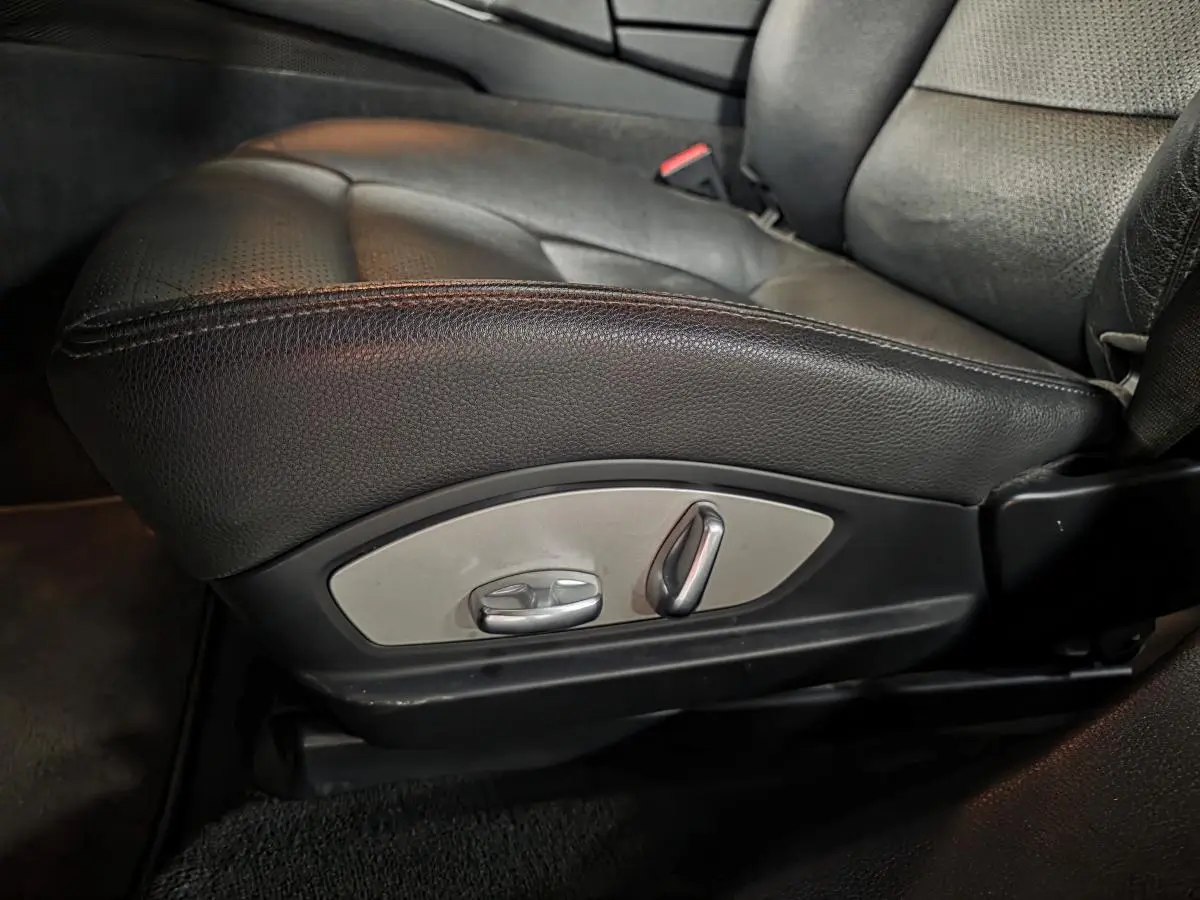 Gros plan sur le siège avant gauche en cuir noir avec commandes électriques de réglage sur une Porsche Panamera marron.