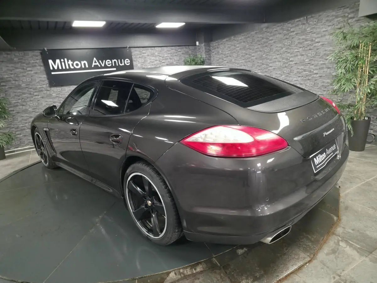 Vue 3/4 arrière droite d'une Porsche Panamera marron métallisée avec jantes noires 20 pouces et sorties d'échappement doubles.