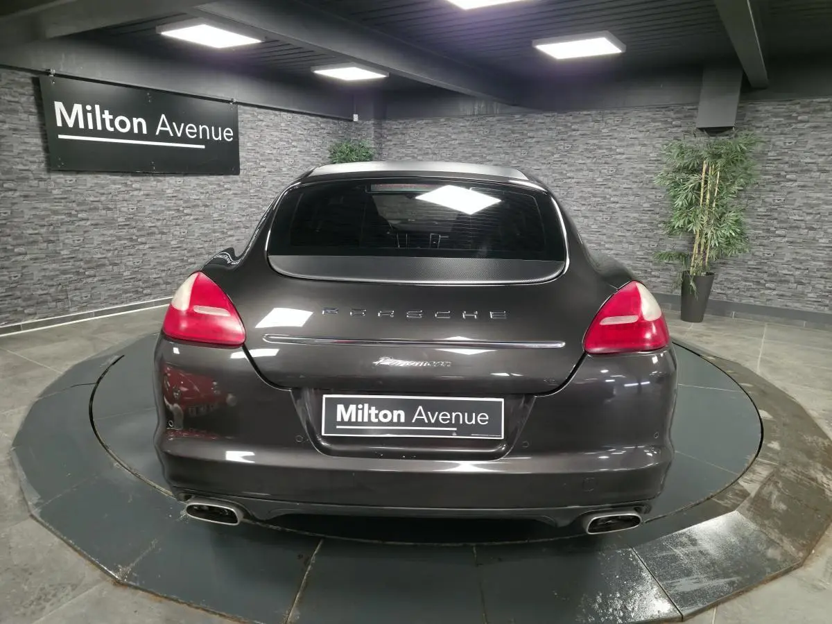 Vue arrière d'une Porsche Panamera marron métallisé avec double sortie d'échappement et hayon chromé dans un showroom.