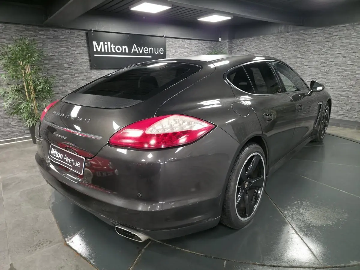 Vue 3/4 arrière droite d'une Porsche Panamera marron métallisée avec jantes noires sport et double sortie d'échappement.