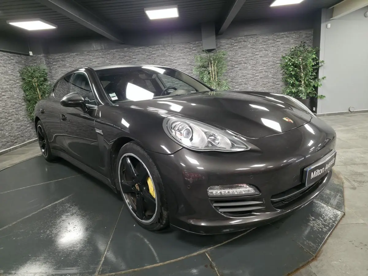 Porsche Panamera marron vue 3/4 avant droit, jantes noires sport 20 pouces et feux de jour à LED visibles.