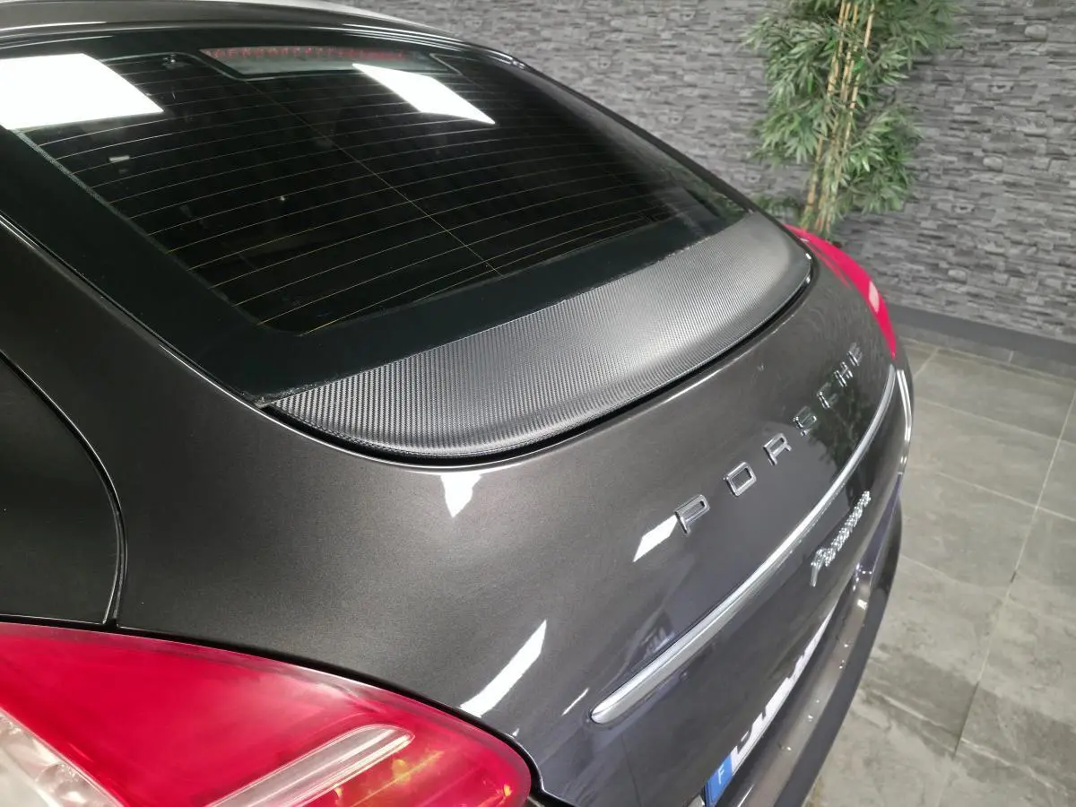 Vue arrière en léger angle droit d'une Porsche Panamera marron métallisée avec aileron carbone et feux rouges.