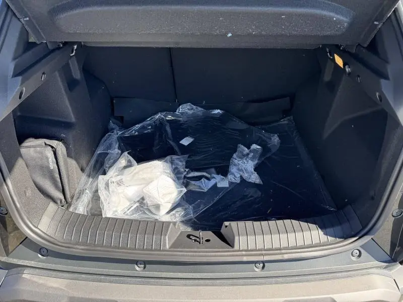 Coffre ouvert du Dacia Duster blanc, vue de l'arrière montrant un espace de chargement vide avec tapis plastique.