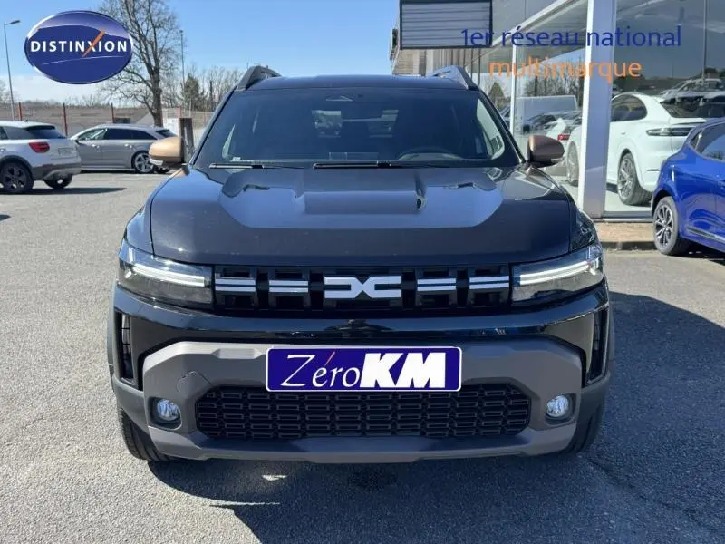 Vue avant d'un Dacia Duster noir avec calandre distinctive et phares LED, stationné en extérieur devant un showroom.