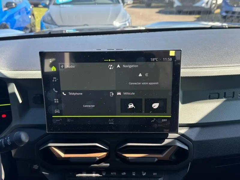 Vue intérieure centrée sur l'écran tactile du tableau de bord du Dacia Duster blanc avec aérateurs hexagonaux noirs et bronze.