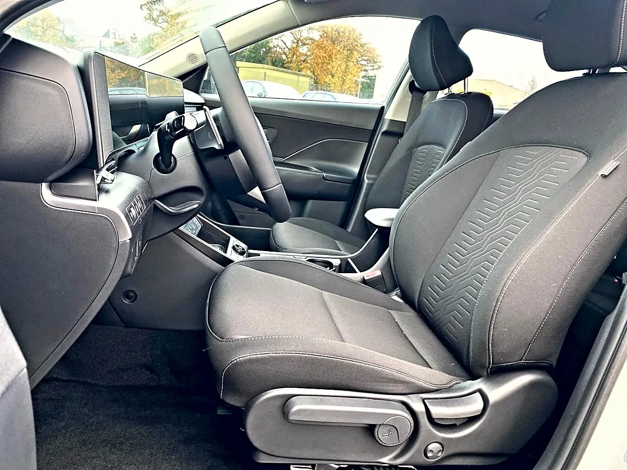 Vue intérieure côté conducteur du Hyundai Kona 2025 gris, avec sièges tissu et volant multifonction cuir.
