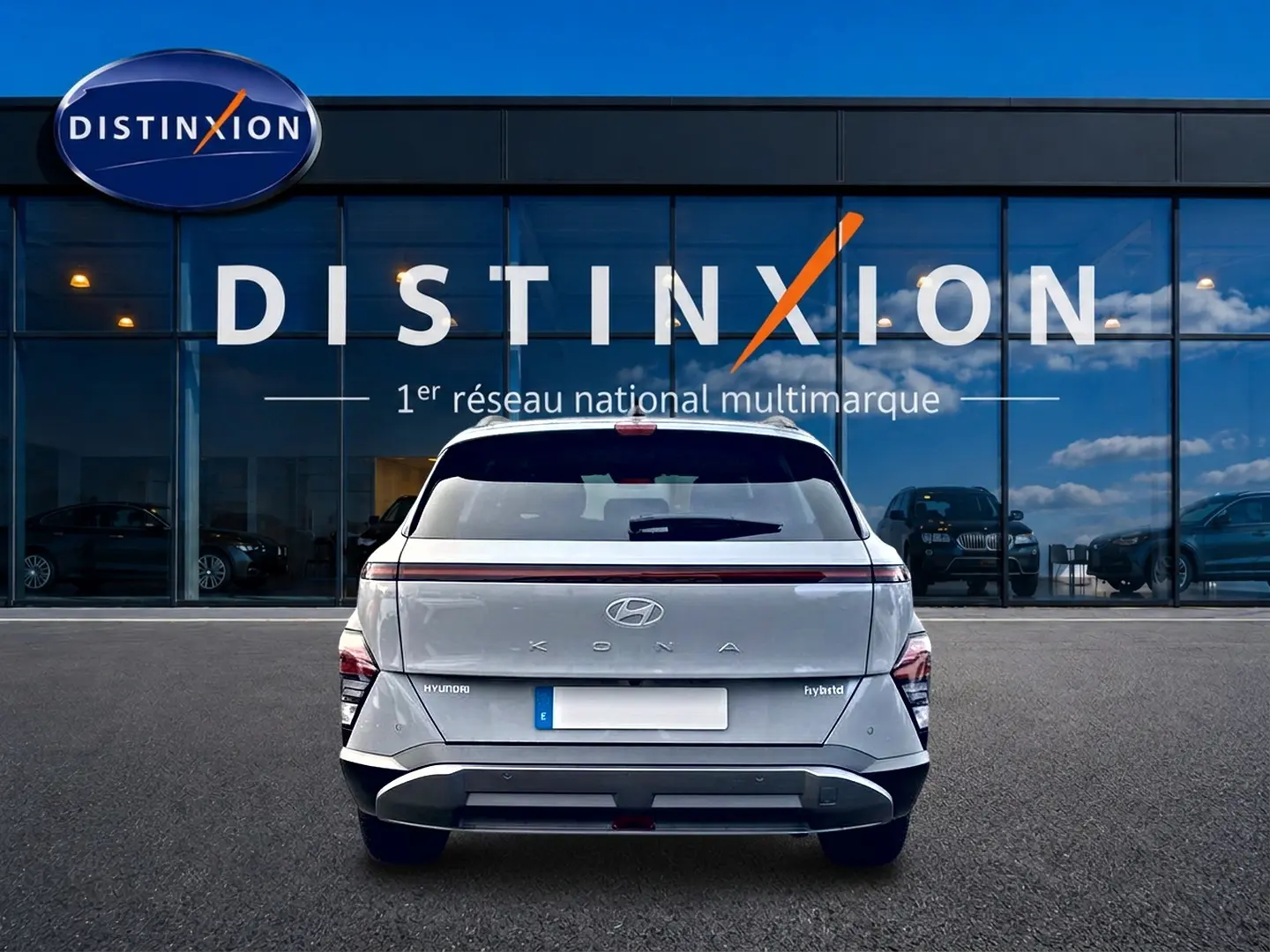 Vue arrière d'un Hyundai Kona gris 2025 avec bande lumineuse LED et logo Hyundai visible, devant une vitrine Distinxion.
