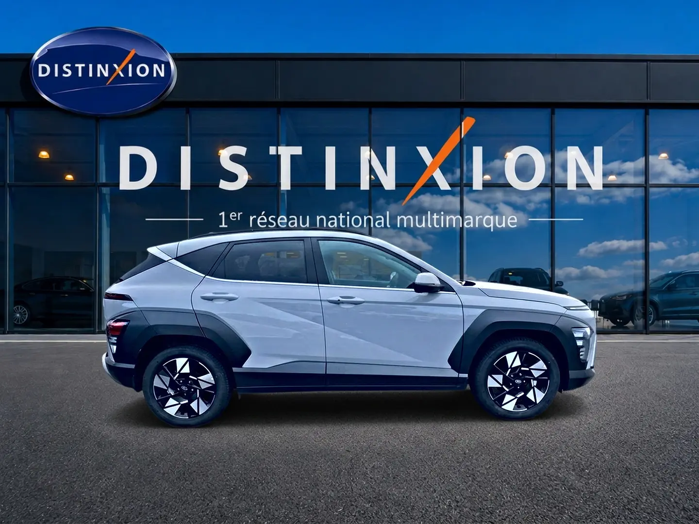 Vue latérale droite d'un Hyundai Kona gris 2025 avec protections noires et jantes alliage distinctives devant une vitrine Distinxion.