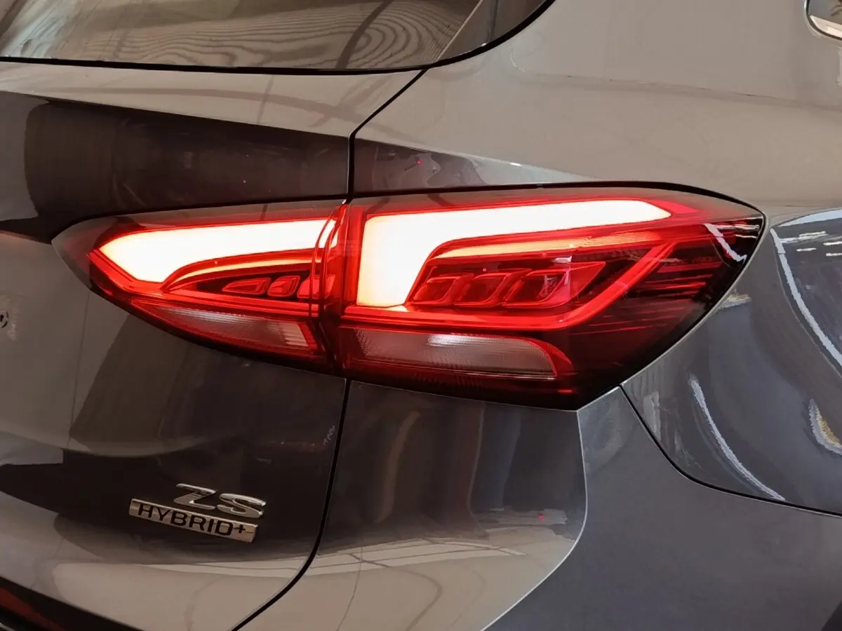 Gros plan sur le feu arrière droit rouge allumé d’un MG Motor ZS gris foncé avec logo Hybrid+ visible.
