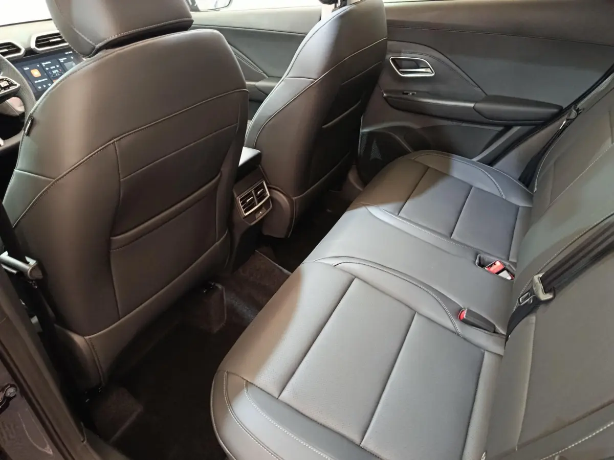 Vue intérieure arrière du MG Motor ZS 1.5L Hybrid+ Luxury 2026, sièges en cuir gris foncé avec accoudoir central.