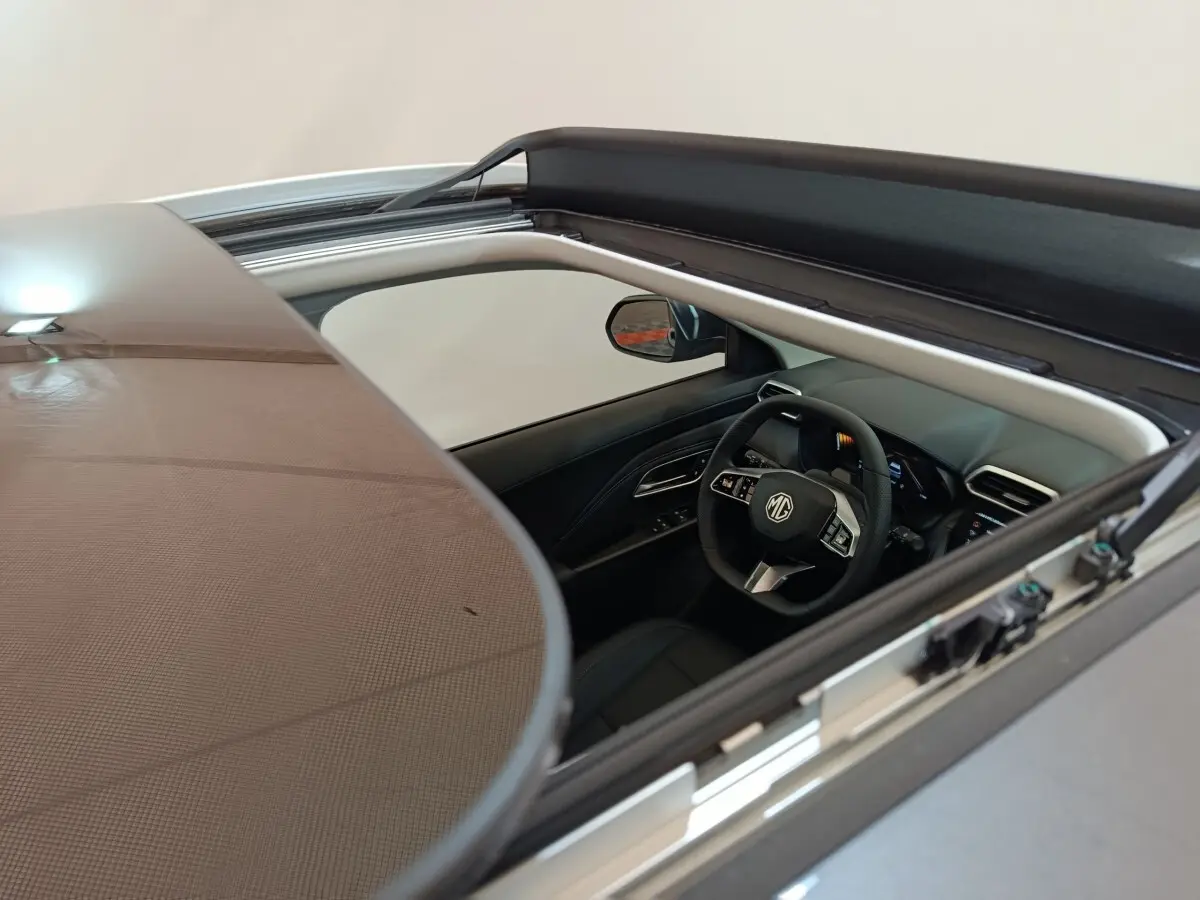 Vue intérieure par le toit ouvrant du MG ZS gris foncé, mettant en valeur le volant multifonctions et le tableau de bord moderne.