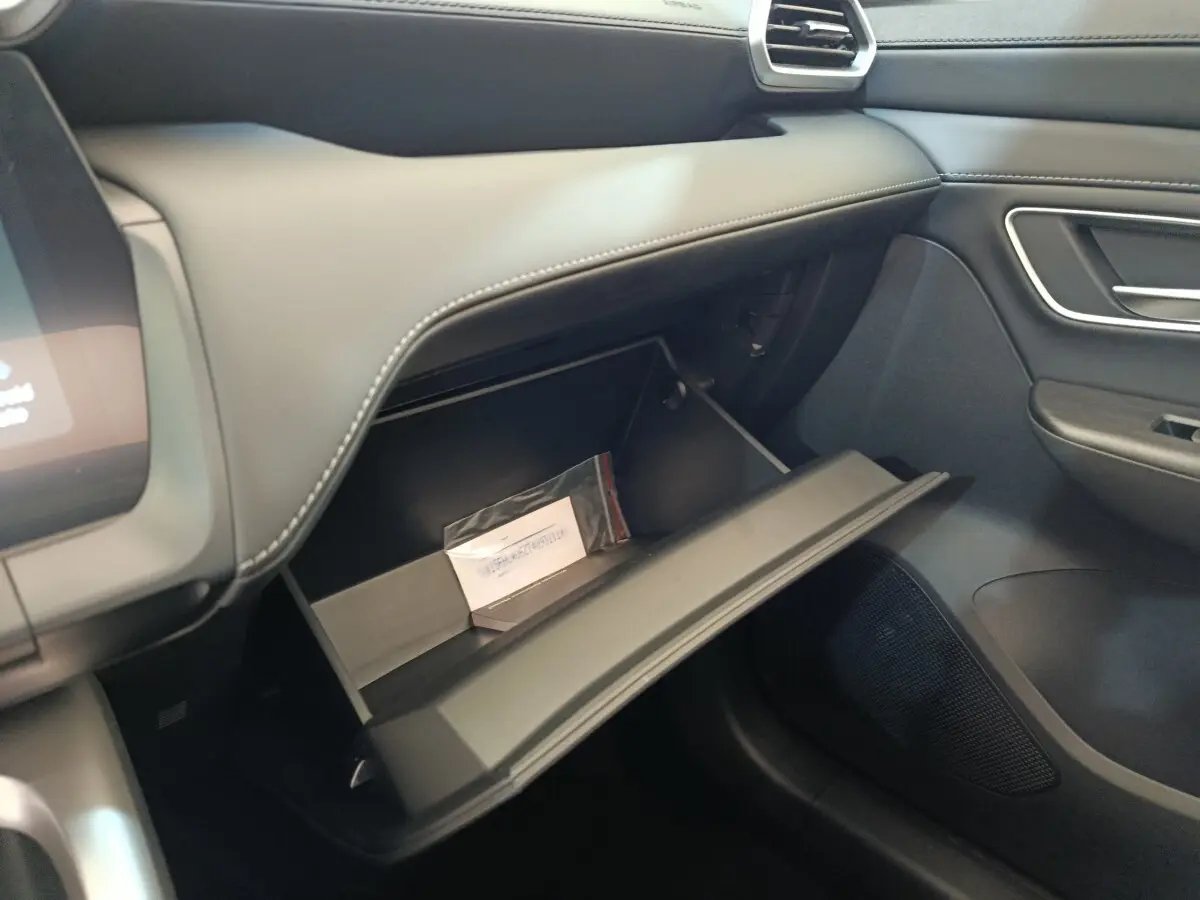 Intérieur MG ZS 2026, vue côté passager sur boîte à gants ouverte avec tableau de bord gris foncé et coutures apparentes.