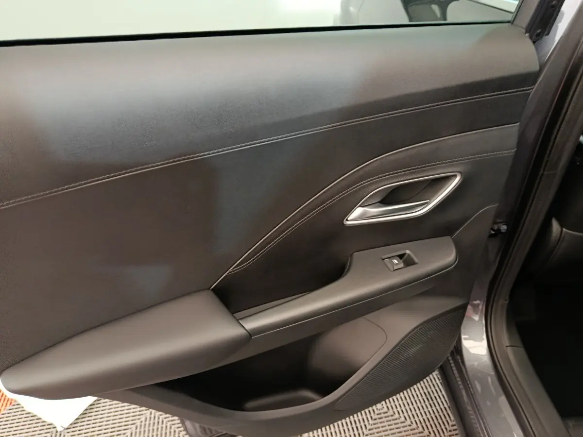 Gros plan sur la porte intérieure côté droit du MG Motor ZS gris foncé, avec poignée argentée et bouton de vitre électrique.