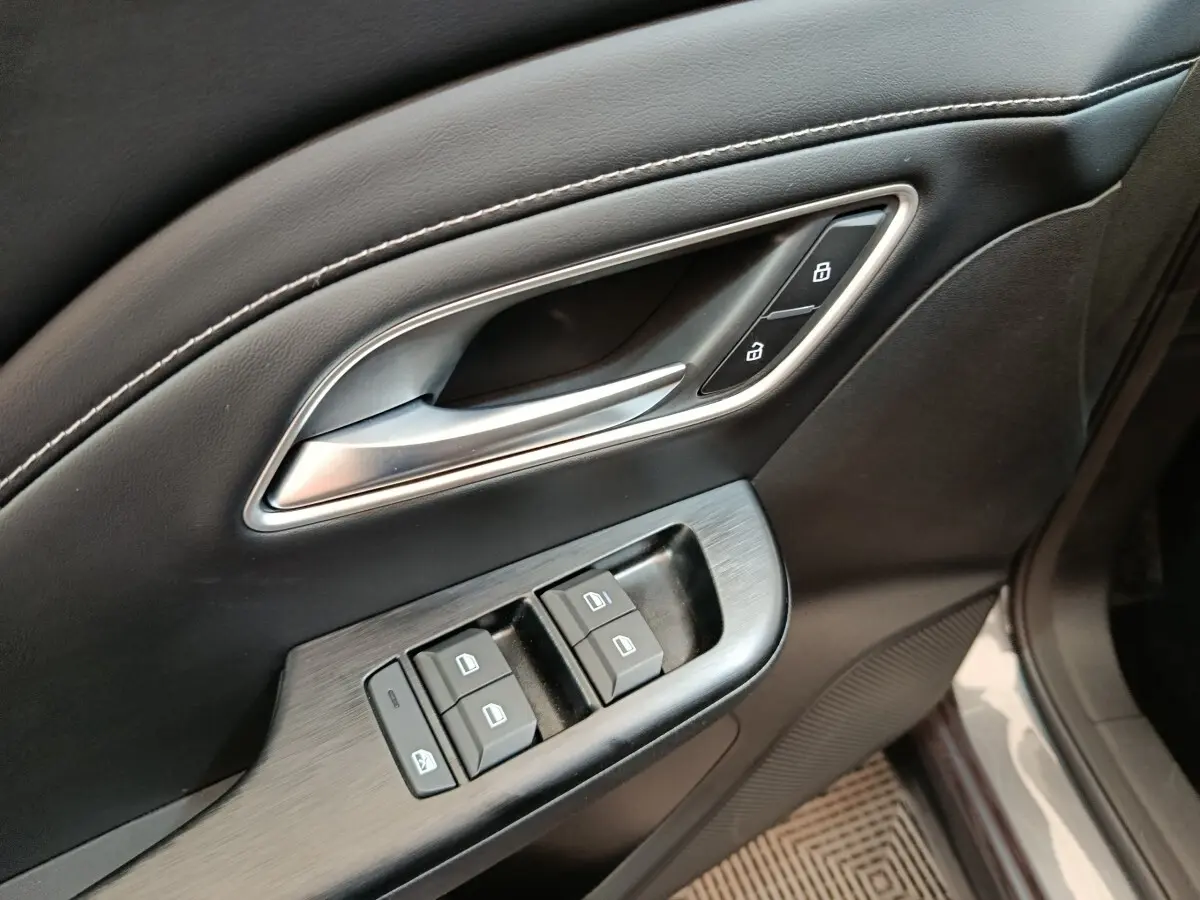 Gros plan sur la commande des vitres et la poignée de porte intérieure en cuir noir du MG MOTOR ZS gris foncé.