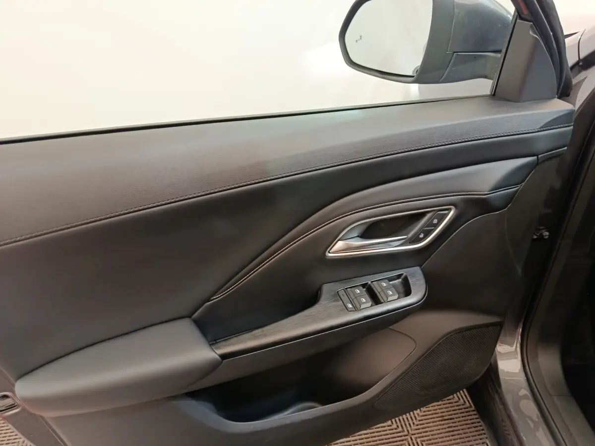 Vue intérieure côté gauche de la porte avant gris foncé du MG MOTOR ZS 1.5L Hybrid+ Luxury avec commandes fenêtres et poignée chrome.