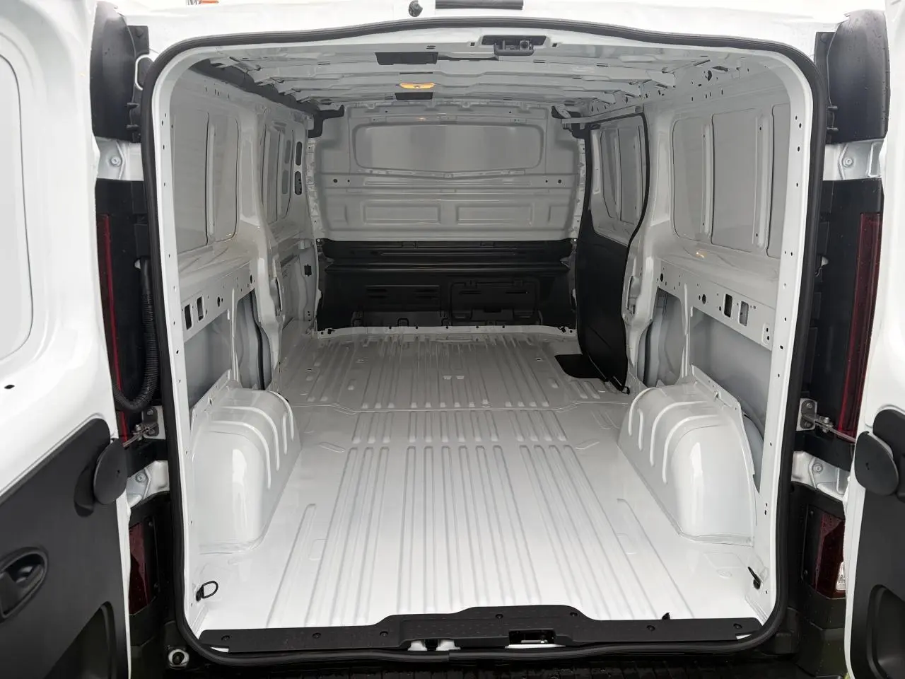 Vue arrière ouverte du Renault Trafic Fourgon blanc glacier, montrant l’espace de chargement vide et tôlé.