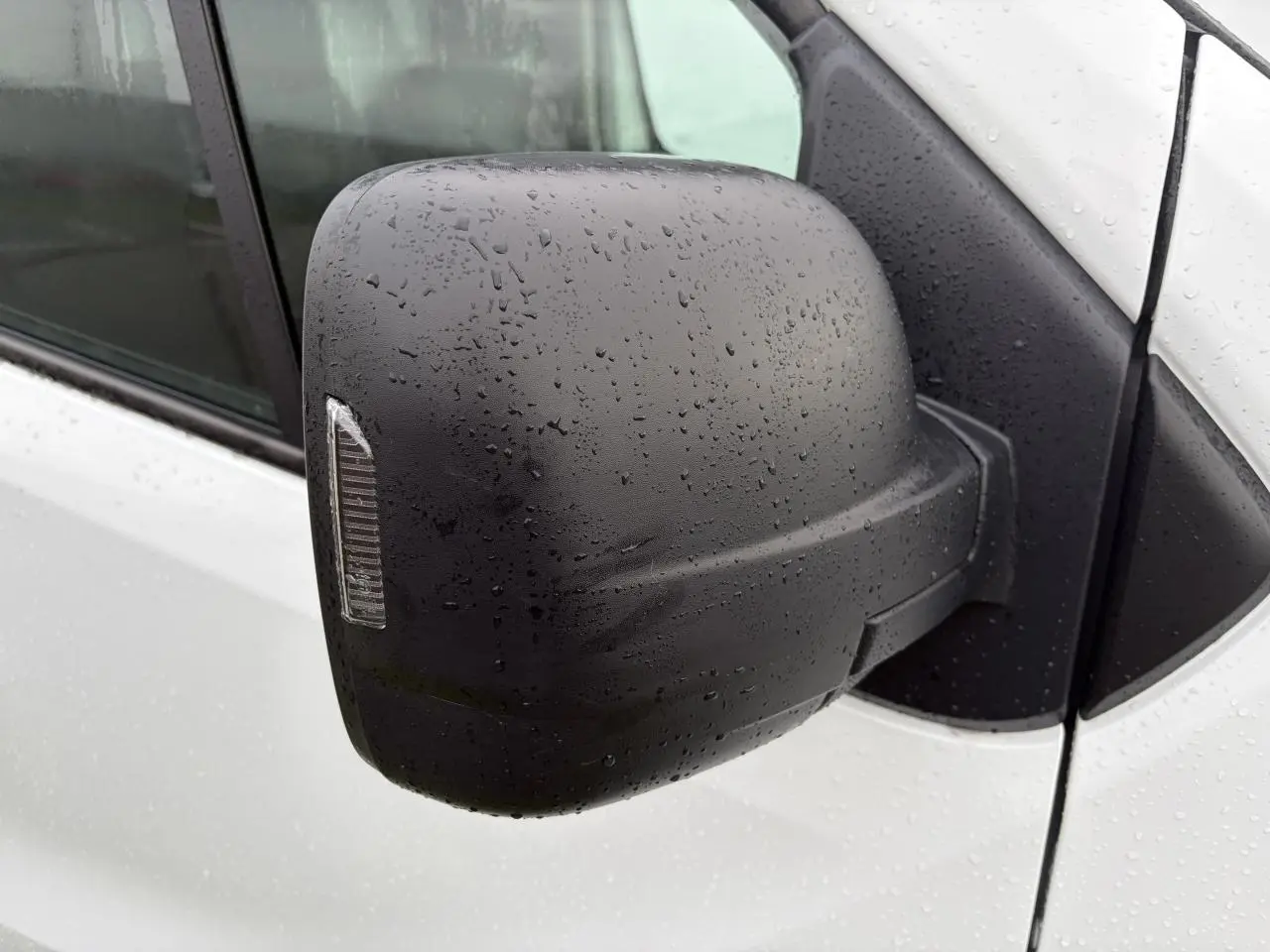 Rétroviseur droit noir avec clignotant intégré sur Renault Trafic blanc glacier sous la pluie.
