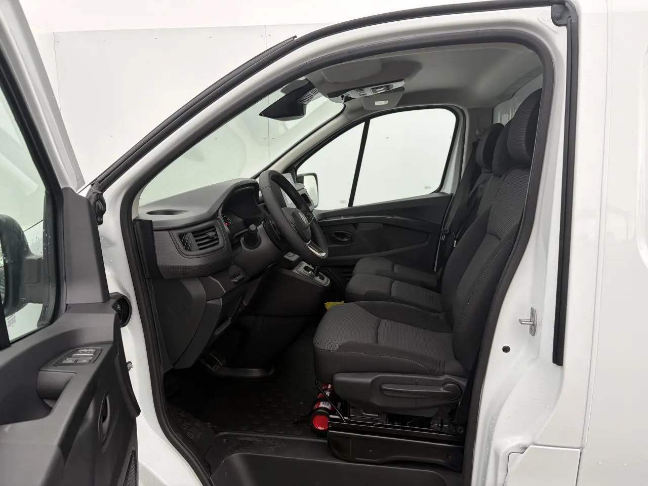 Vue intérieure côté conducteur du Renault Trafic Fourgon blanc glacier 2025, montrant les sièges avant et le tableau de bord.