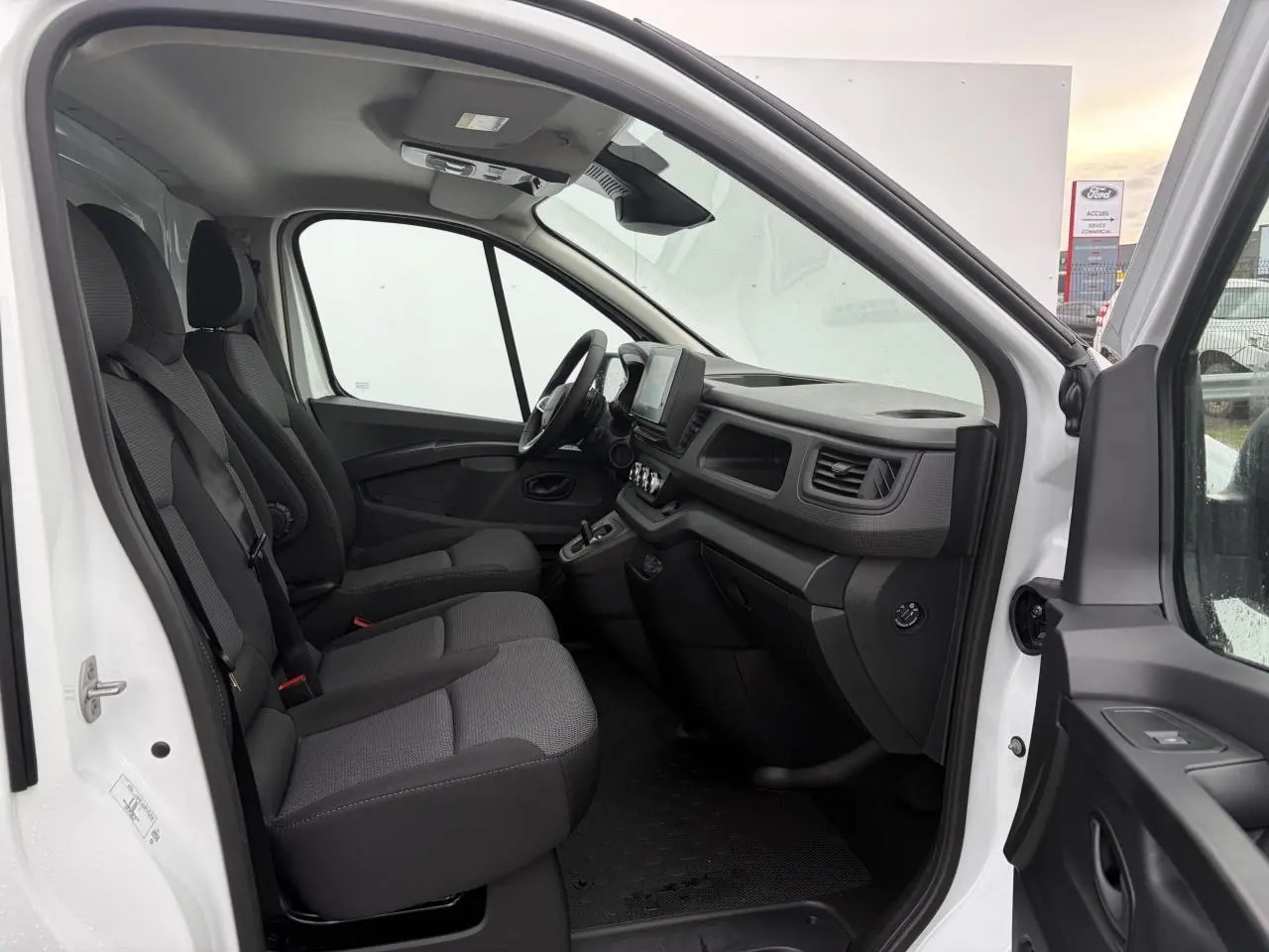 Vue intérieure côté conducteur du Renault Trafic Fourgon blanc glacier, montrant les sièges tissu Kompo et le tableau de bord avec écran tactile.