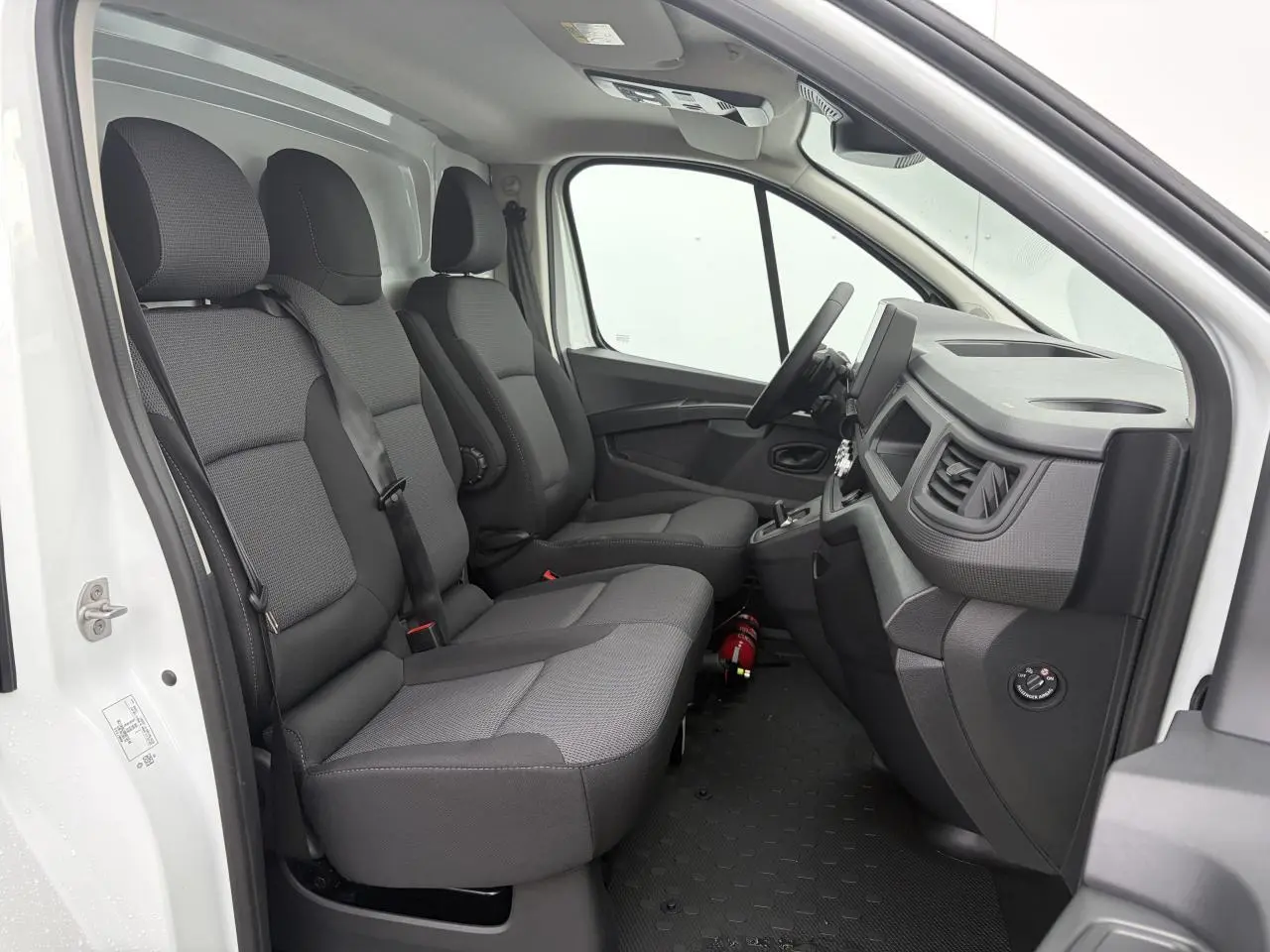 Vue intérieure côté conducteur du Renault Trafic Fourgon blanc Glacier, montrant la banquette passager et le tableau de bord gris.