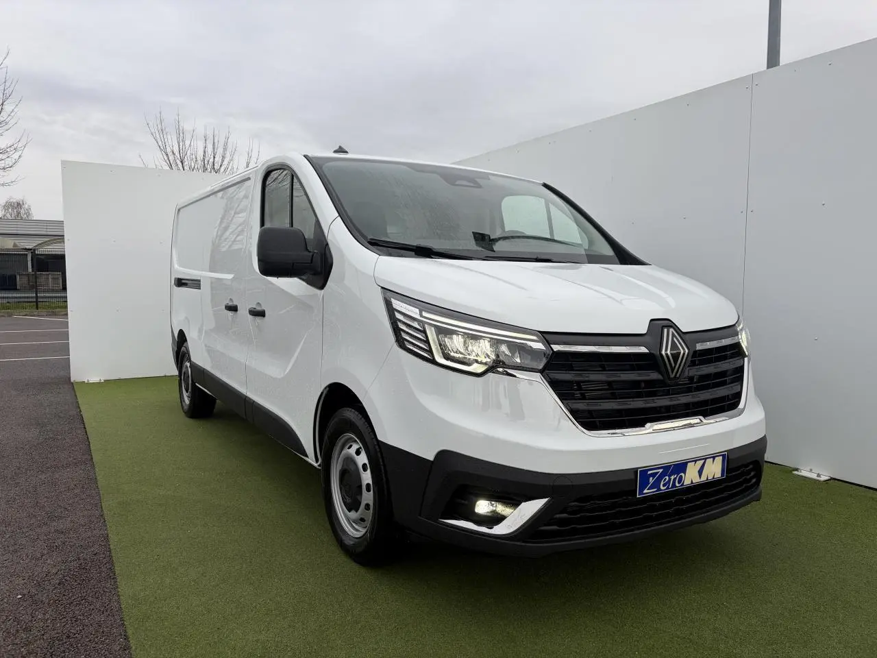Renault Trafic Fourgon blanc glacier vu en 3/4 avant droit, avec projecteurs LED allumés et jantes tôles.