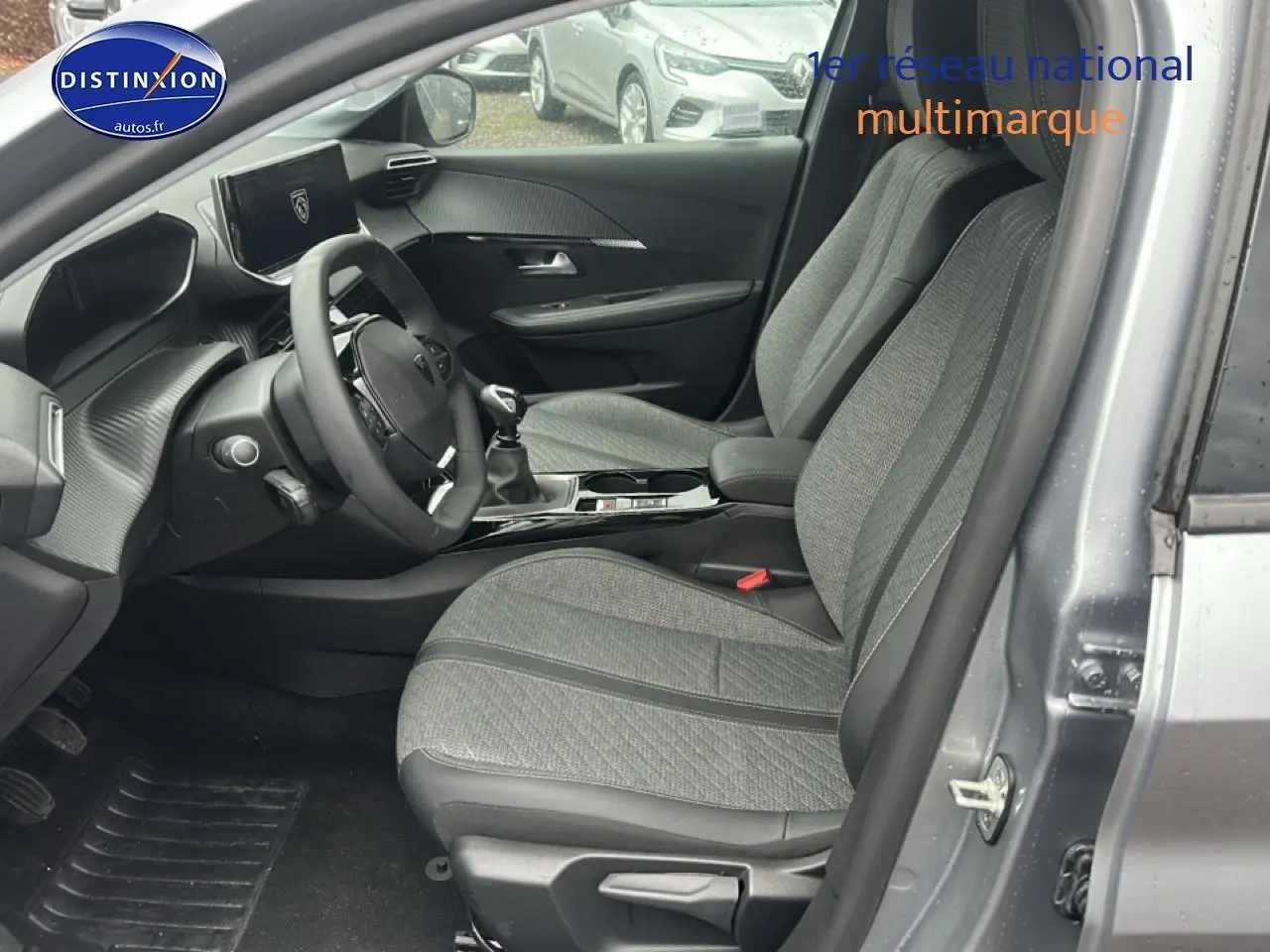 Vue intérieure côté conducteur de la Peugeot 208 1.2 PureTech 100 Allure gris Artense avec sièges tissu gris et console centrale noire.