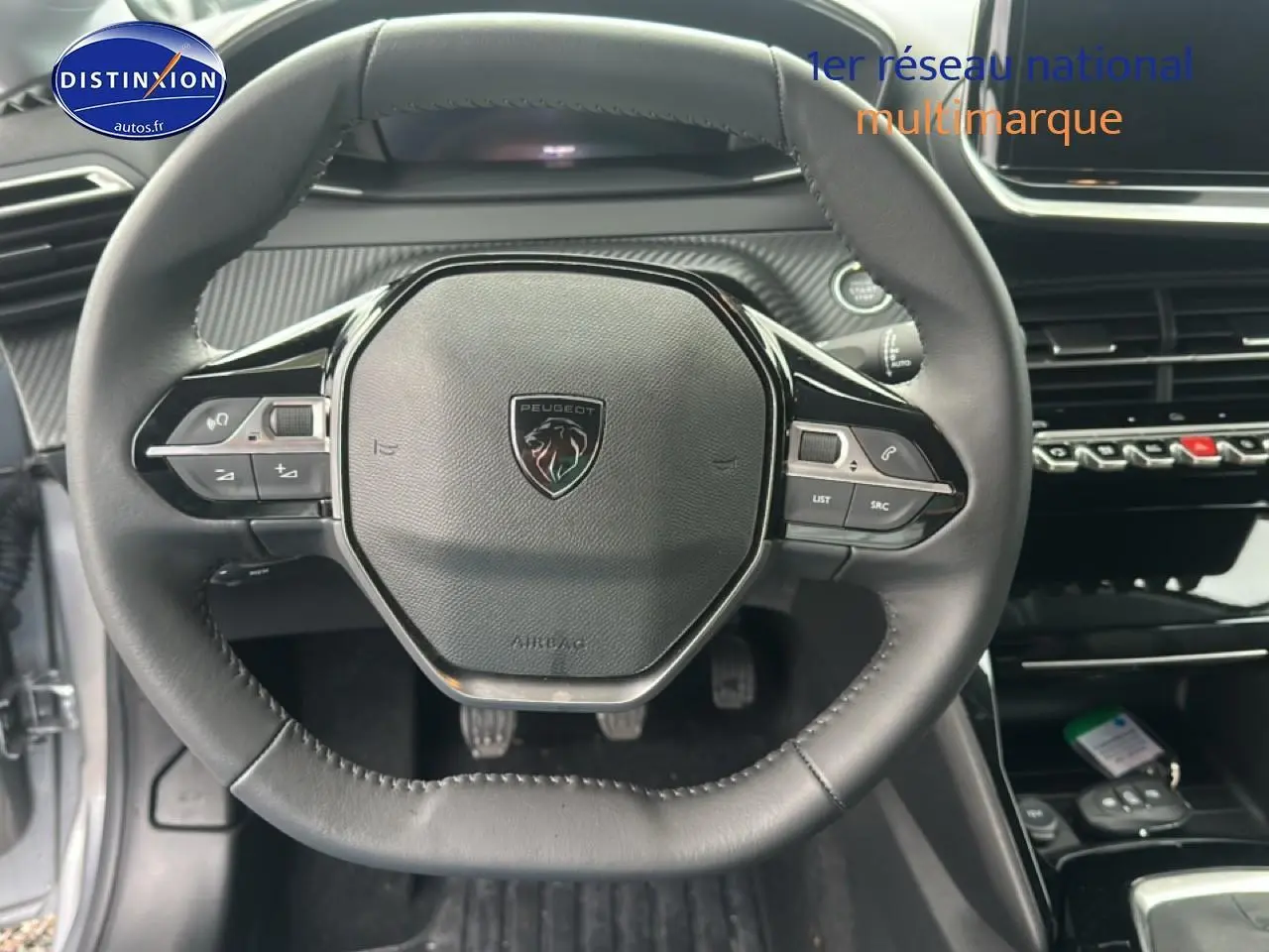 Vue rapprochée du volant cuir noir de la Peugeot 208 2024 avec commandes intégrées et logo central.