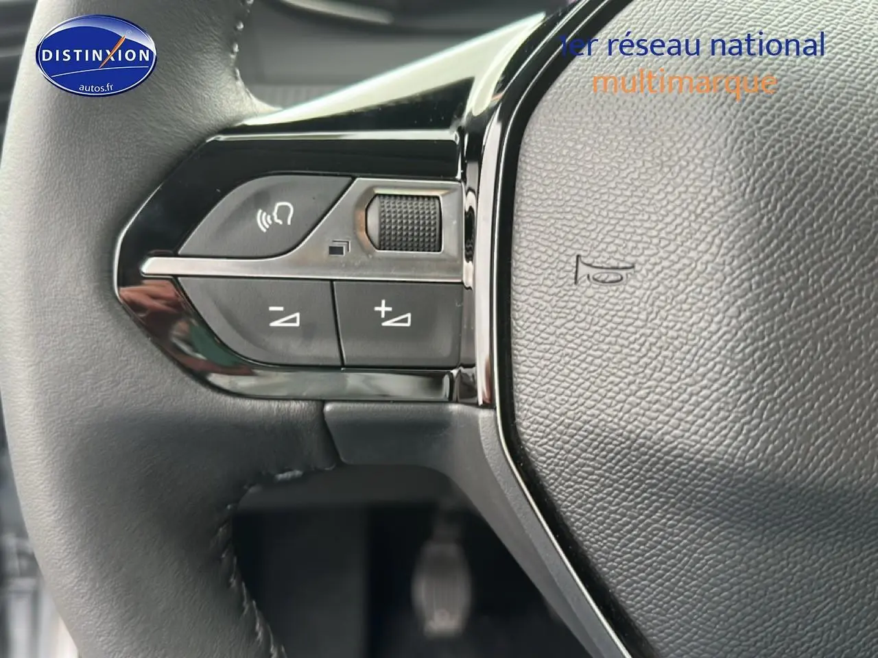 Gros plan sur les commandes de volume au volant noir de la Peugeot 208 1.2 PureTech 100 Allure 2024.