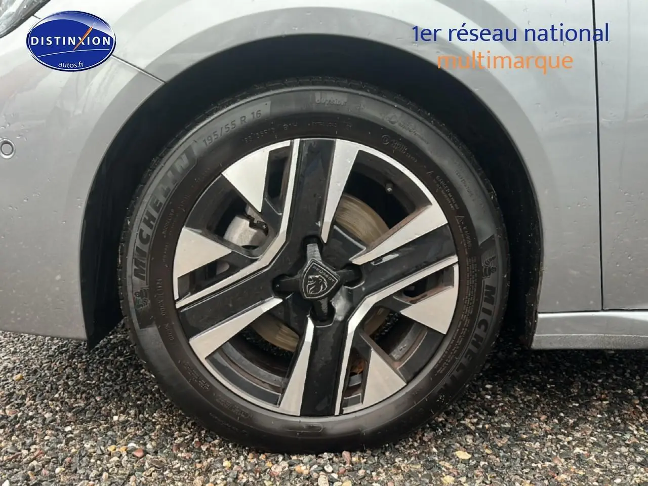 Gros plan sur la roue avant gauche d'une Peugeot 208 gris artense avec jante alu au design moderne.