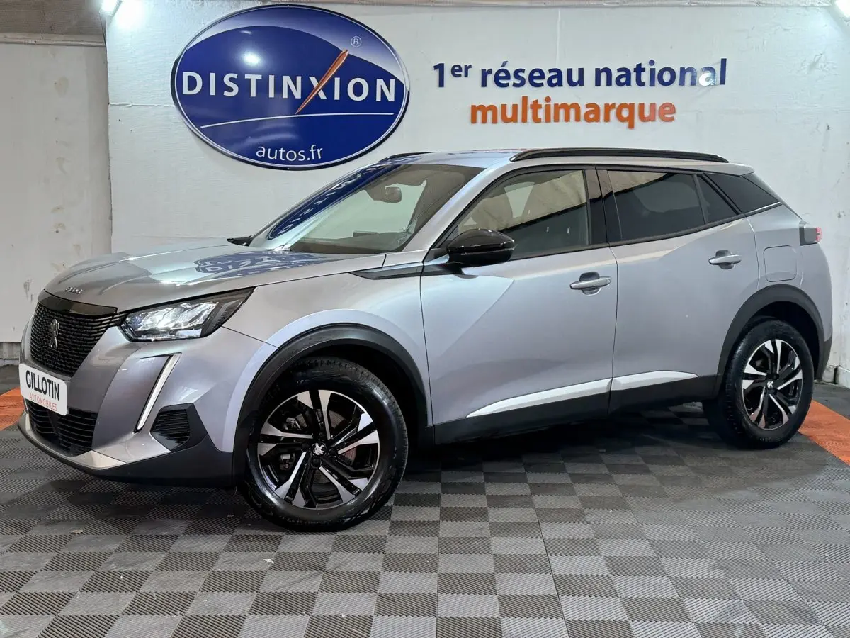 Peugeot 2008 gris clair en vue 3/4 avant droit, avec jantes noires et toit noir contrasté en intérieur showroom.