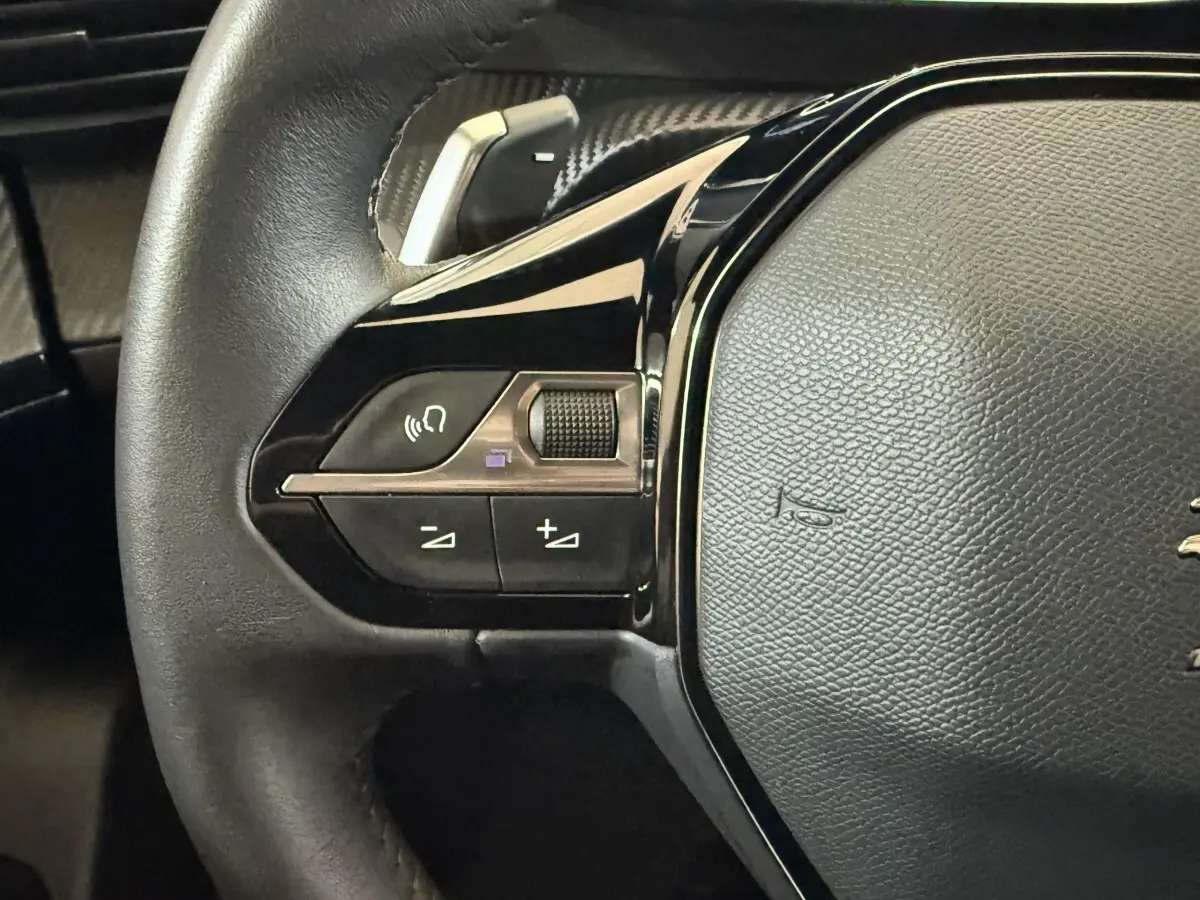 Gros plan sur le côté gauche du volant cuir noir du Peugeot 2008 gris clair, avec commandes multifonctions intégrées.