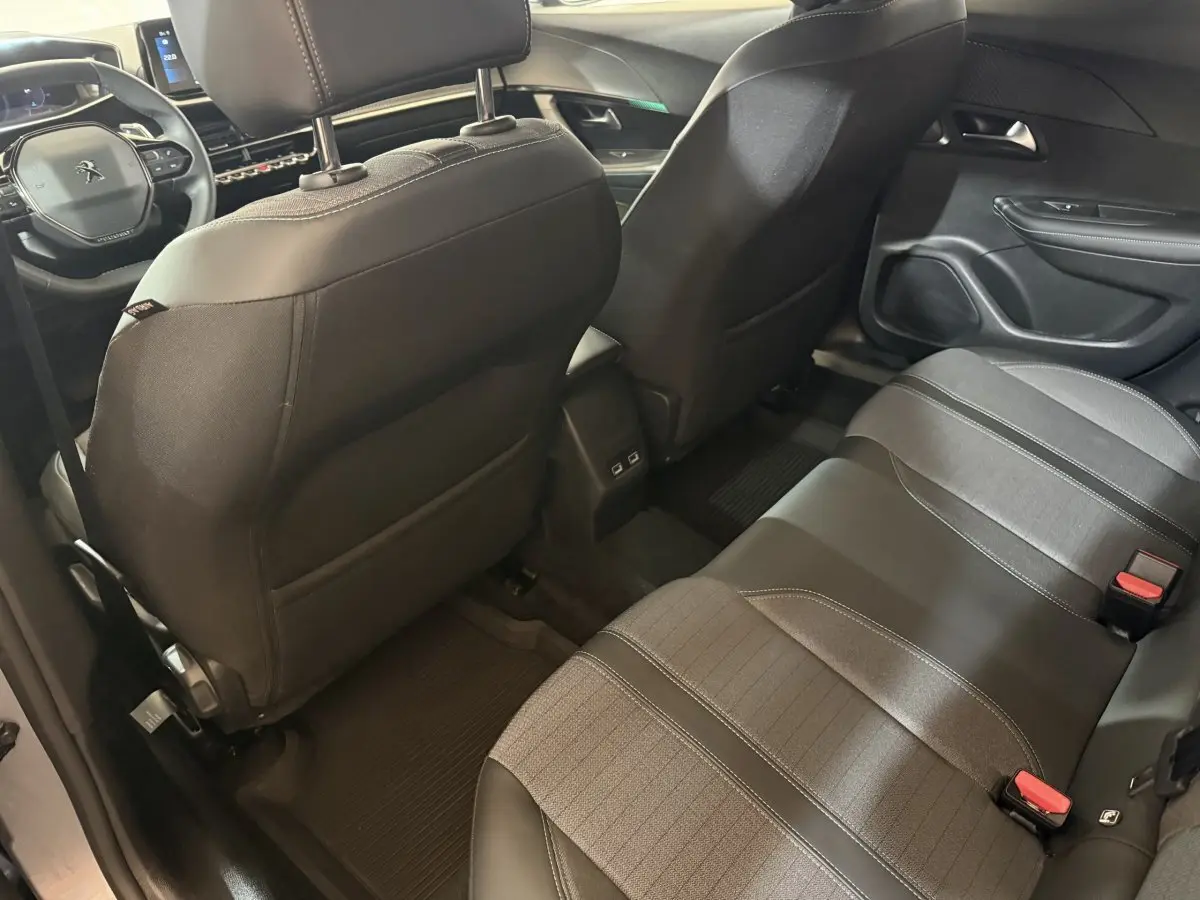 Vue intérieure arrière du Peugeot 2008 gris clair 2023, montrant les sièges tissu et cuir et le tableau de bord avant.