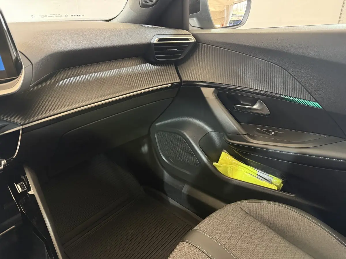 Vue intérieure côté passager avant du Peugeot 2008 gris clair, avec tableau de bord à effet carbone et porte avec rangement.