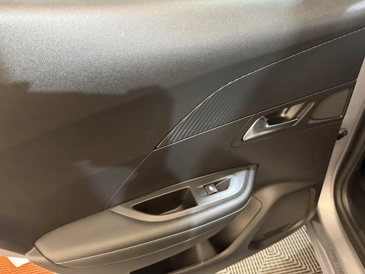Vue intérieure côté droit de la porte avant grise claire du Peugeot 2008 avec poignée argentée et commande de vitre.