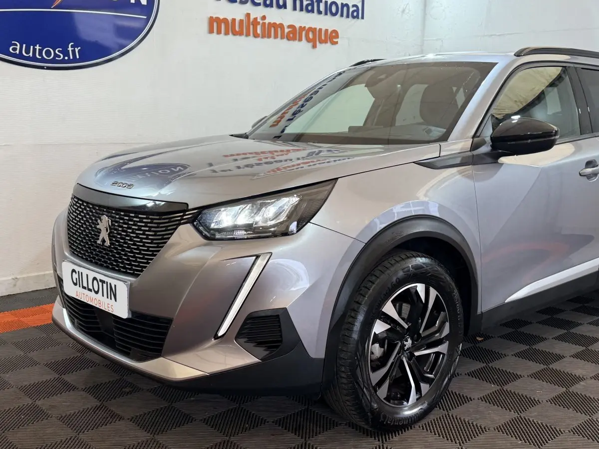 Peugeot 2008 gris clair en 3/4 avant droit, avec calandre noire et phares LED distinctifs.