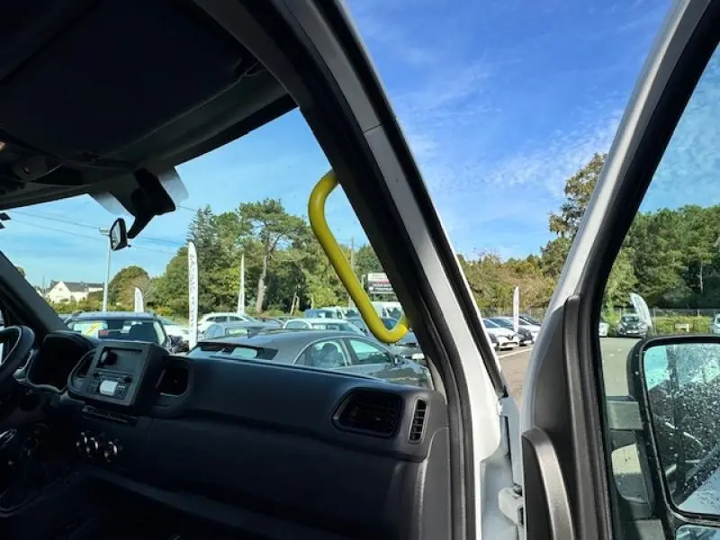 Vue intérieure côté conducteur du Renault Master Combi blanc minéral, mettant en valeur la poignée d'accès jaune TPMR et le tableau de bord.