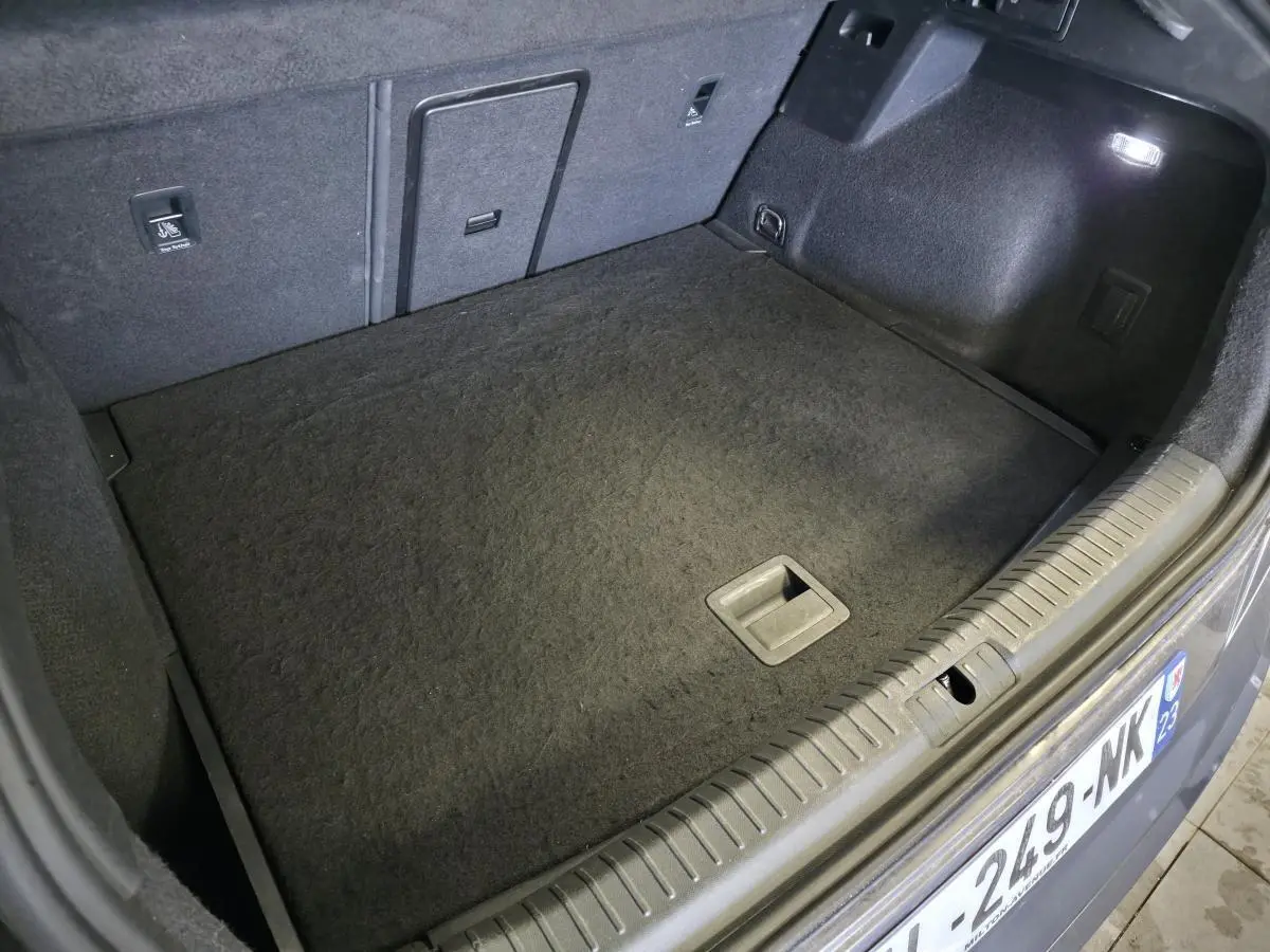 Coffre ouvert du CUPRA Formentor bleu, vue plongeante sur le tapis de sol et hayon électrique avec éclairage intérieur.