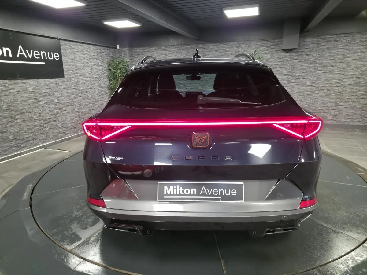 Vue arrière d'un CUPRA Formentor bleu avec bandeau lumineux LED et double sortie d'échappement noire dans un showroom.