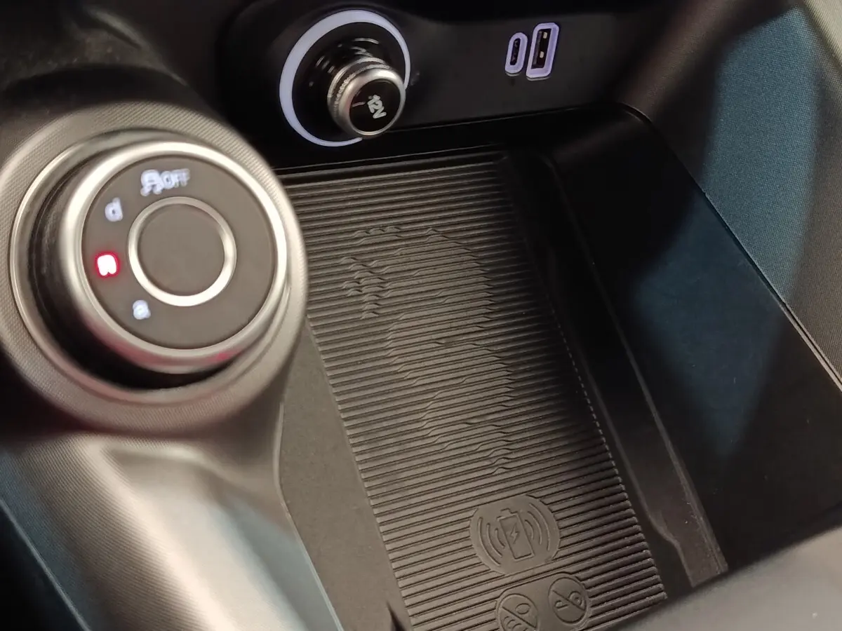 Gros plan sur la console centrale de l'Alfa Romeo Tonale bleu, montrant la molette de sélection et la zone de recharge sans fil.