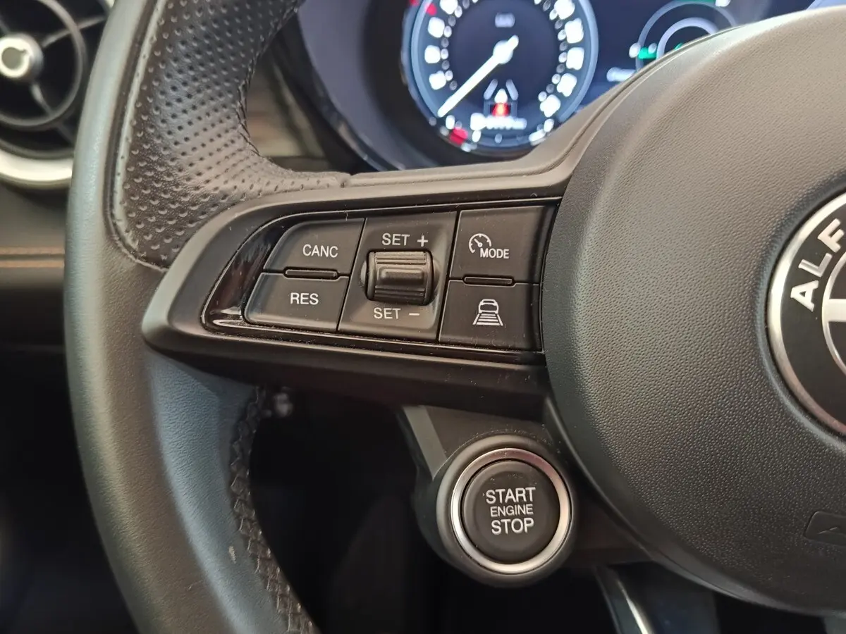 Gros plan sur le volant cuir noir de l'Alfa Romeo Tonale bleu, avec commandes de régulateur et bouton démarrage.